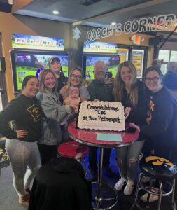 Group of Coach's Corner staff with a regular customer holding a cake for a retirement celebration