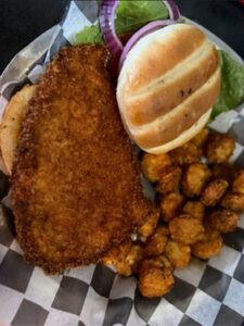 Breaded pork tenderloin sandwich served on a bun with tater tots