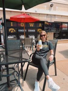 Woman sitting at a table on the Coach's Corner patio holding out a Carbliss drink